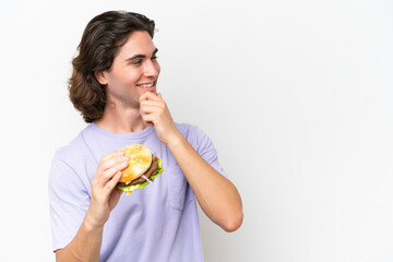 Young handsome man holding a burger isolated on white background thinking an idea and looking side
