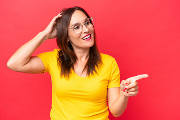 Middle-aged caucasian woman isolated on red background surprised and pointing finger to the side