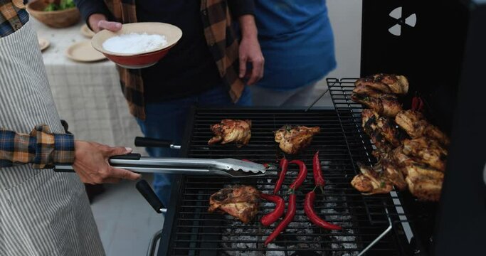 Multi generational people doing barbecue during weekend day at home's rooftop preparing food - Multiracial friends having fun together - Mature asian woman cooking chili and chicken on bbq grill