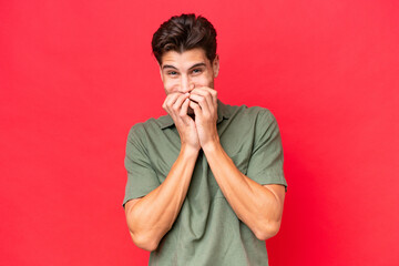 Young caucasian handsome man isolated on red background happy and smiling covering mouth with hands