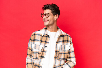 Young caucasian handsome man isolated on red background looking to the side and smiling