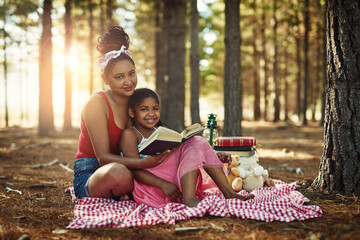 Ensuring her little one stays a keen reader. a mother and her little daughter reading a book together in the woods.