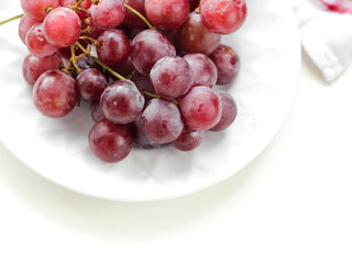 Fresh red grapes fruit in white plate on white background