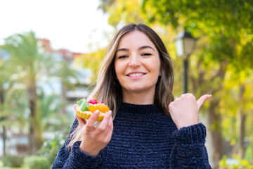 Young pretty Romanian woman holding a tartlet at outdoors pointing to the side to present a product