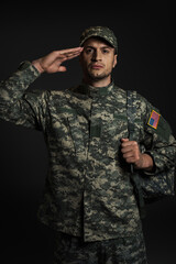 patriotic soldier in uniform with American flag saluting isolated on black.