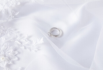 Two wedding rings made of white gold with a diamond lie on a white veil with soft pleats. Wedding background. layout for design. postcard. invitation.