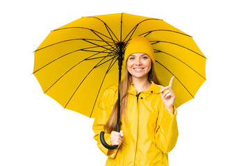 Young blonde woman with rainproof coat and umbrella over isolated chroma key background pointing up...