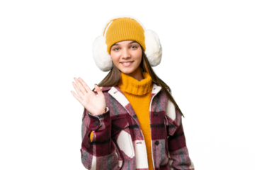 Teenager caucasian girl wearing winter muffs over isolated background saluting with hand with happy expression