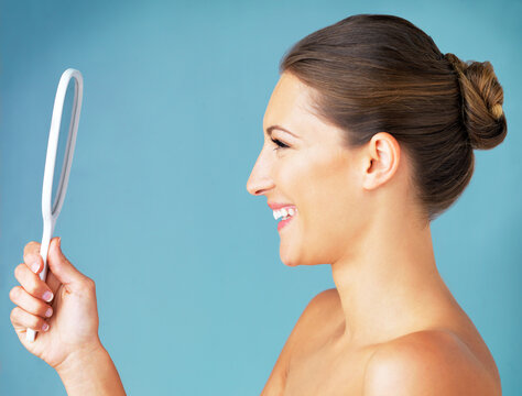 Theres No One Better Than Yourself. Studio Shot Of A Beautiful Young Woman Looking At Herself In The Mirror Against A Blue Background.