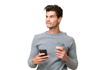 Young handsome caucasian man over isolated background holding coffee to take away and a mobile while thinking something