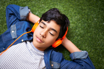 Headphones, music and boy relax on grass with eyes closed outdoors on holiday, free time and...