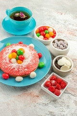 front view yummy pink cake with colorful candies and cup of tea on a white background dessert pie rainbow color cake candy
