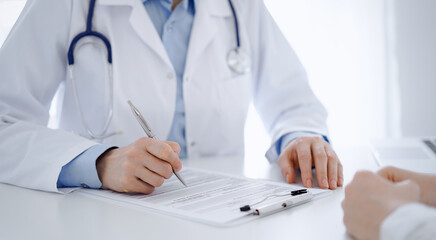 Fototapeta premium Stethoscope lying on the tablet computer in front of a doctor and patient sitting opposite each other at the background . Medicine, healthcare concept