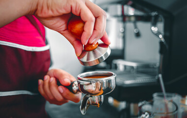 Hand of a barista holding a portafilter and a coffee tamper making an espresso coffee. Barista presses ground coffee using a tamper in a coffee shop