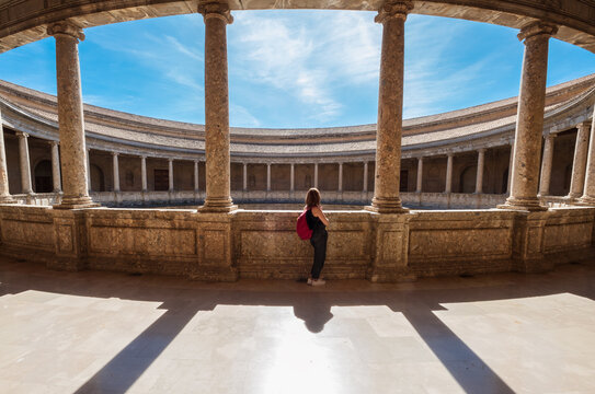 Young female tourist with backpack enjoying wide galleries with columns in the inner circular patio in Palace of Charles V in Alhambra complex in Granada, Andalusia, Spain.