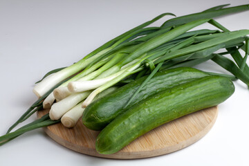 On the table are two cucumbers and green onions. On a white background.