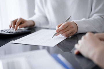 Woman accountant using a calculator and laptop computer while counting taxes for a client. Business audit and finance concepts