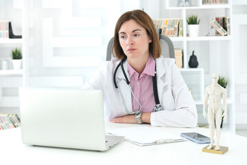 Young attractive female doctor sitting at the desktop in the office and consulting her patient online	