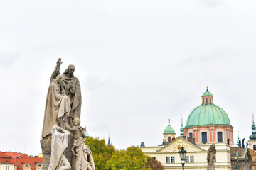 Fototapeta na wymiar Ancient catholic sculptures on a pedestal and old buildings with green dome and towers with the green top. Statues on biblical subjects. Charles Bridge. Prague, Czech Republic, October 2022.
