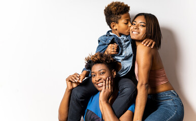 A dark-skinned woman happily poses with a child who gives a teenage girl a kiss on the face on a white background. Single-parent family, cheerful family of 3 Africans on a white background.