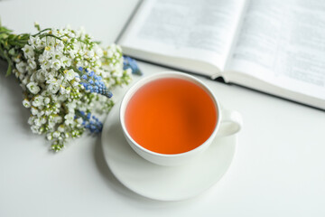 Open bible with flowers and a cup of tea on a white background