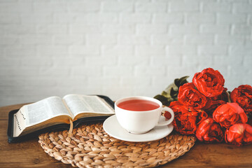 Open bible with tulip flowers and a cup of tea on light wood