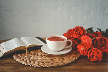 Open bible with tulip flowers and a cup of tea on light wood