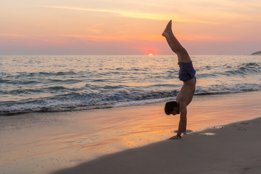 Fit man doing handstand on wet seashore