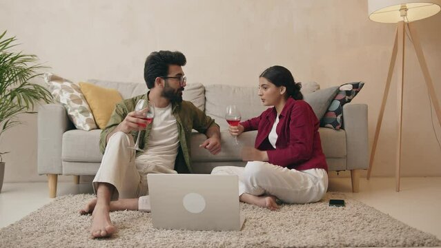 Cheerful couple talking calmly and drinking wine in living room at home