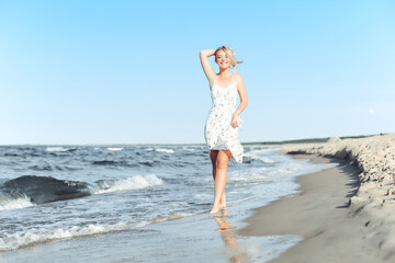 Fototapeta na wymiar Happy blonde woman wearing sun glasses and relaxing on a wooden deck chair at the ocean beach