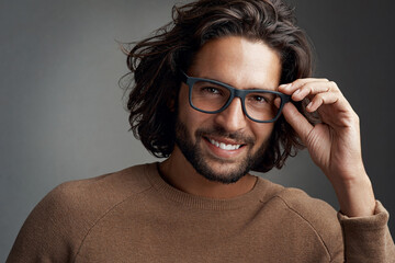 I like what I see. Studio shot of a handsome young man wearing glasses against a gray background.