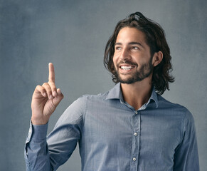 The ad is up there not down here. Studio shot of a handsome young man pointing against a grey background.