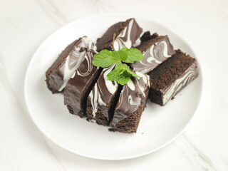 Brownies Kukus or Chocolate Steam Cake Brownies with marble chocolate glaze on top. Served in white ceramics pllate. Selective focus, white background
