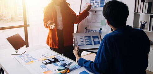 Close up ux developer and ui designer brainstorming about mobile app interface wireframe design on table with customer breif and color code at modern office.Creative digital development agency
