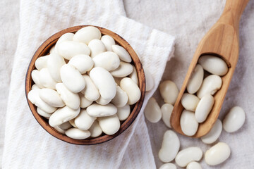 White beans in wood bowl with scoop on linen cloth background