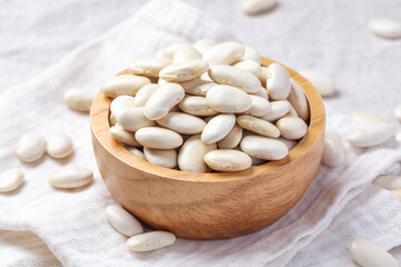 White beans in wood bowl with spoon on linen cloth