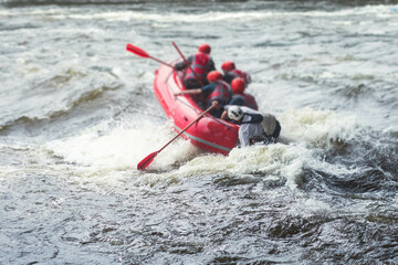 Fototapeta na wymiar Red raft boat during whitewater rafting extreme water sports on water rapids, group of sportsmen in wetsuits kayaking and canoeing on the river, water sports team with a big splash of water
