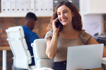 Young Smiling Businesswoman Working At Desk In Office Talking On Mobile Phone