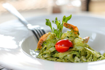 Tagliatelle pasta with shrimps and pesto sauce in white plate.