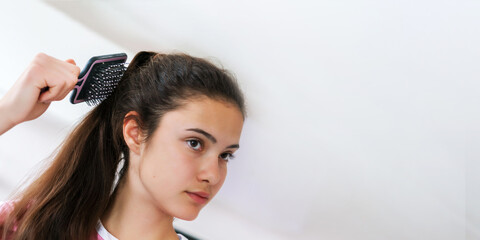 Fototapeta premium schoolgirl brushes long ponytail with stylish hairbrush against bathroom wall in morning close view