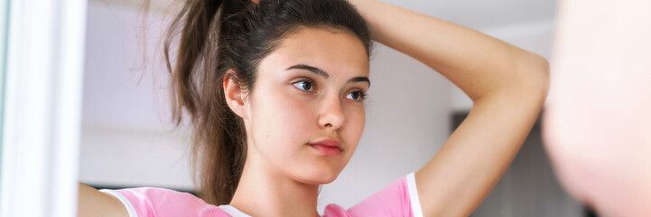 teenage brunette makes hairstyle reflecting in large mirror in bathroom with white walls in morning close view