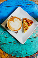 Cappuccino coffee and apple pie on colorful green and blue cafe table