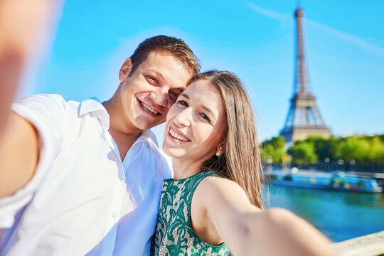 Young romantic couple taking funnyselfie with mobile phone near the Eiffel tower in Paris, France