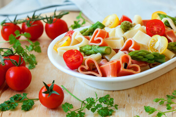 Romantic dinner. Delicious heart-shaped pasta with tomatoes, asparagus and fresh herbs