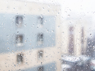 trickles of rain flowing down on surface of window glass in city apartment and view of urban house on background