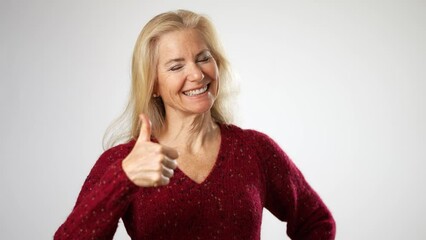 Giving a thumbs up, a pretty attractive mature blond woman in red sweater smiling happy portrait isolated on solid white background with copy space.