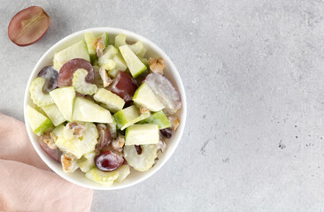 Bowl of waldorf salad with apple, celery, grapes, walnuts and yogurt on a gray background. Top view. Copy space.