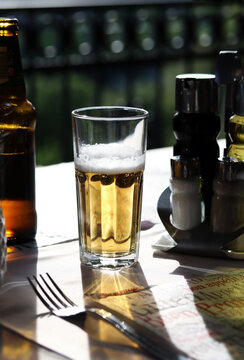 Glass of cold light beer with foam on the restaurant table. Real life photography at a restaurant, sunny day, light cold beer on the table, close up.
