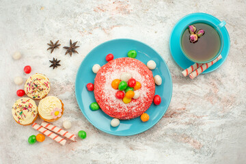 Obraz na płótnie Canvas top view tasty pink cake with candies and cup of tea on white background goodies rainbow candy dessert color cake