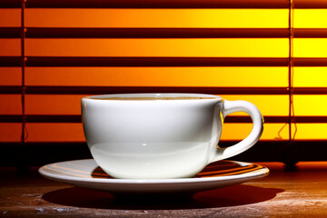 coffee cup filled with frothy coffee set against a window blind